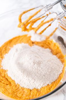 Mixing ingredients in a large glass mixing bowl to bake pumpkin bunt cake.