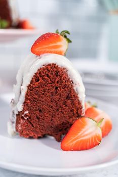 Slice of red velvet bundt cake with cream cheese frosting garnished with fresh strawberries on a white plate.