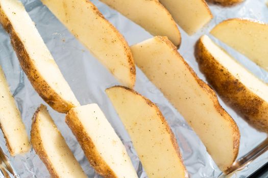Preparing russet potatoes in wedges with olive oil and spices to bake in the oven.