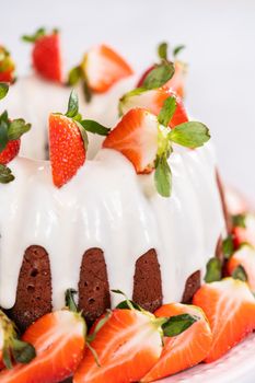 fresh strawberries..Red velvet bundt cake with cream cheese frosting garnished with fresh strawberries on a pink cake stand for Valentines Day.