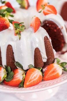 Slicing red velvet bundt cake with cream cheese frosting garnished with fresh strawberries.