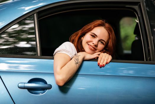 Portrait of of young woman looking at camera through window and sitting at the back seat in the car