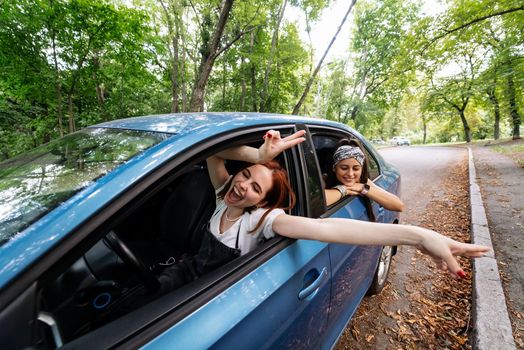 Two attractive young girlfriends fool around and laughing together in a car on a sunny day.