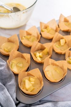 Scooping dough into the cupcake pan lined with parchment muffin liners to bake sharlotka muffins.