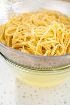 Draining water from linguine pasta through a mesh strainer.
