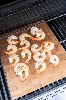 Grilling shrimp on a grill mat over an outdoor gas grill.