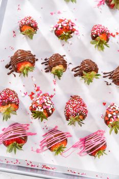 Decorating chocolate-covered strawberries with chocolate drizzles and sprinkles.