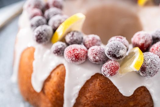 Lemon cranberry bundt cake decorated with sugar cranberries and lemon wedges on a cake stand.