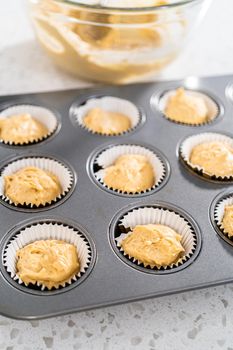 Scooping cupcake batter with dough scoop into a baking cupcake pan with liners to bake dulce de leche cupcakes.