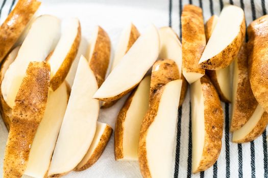 Preparing russet potatoes in wedges with olive oil and spices to bake in the oven.