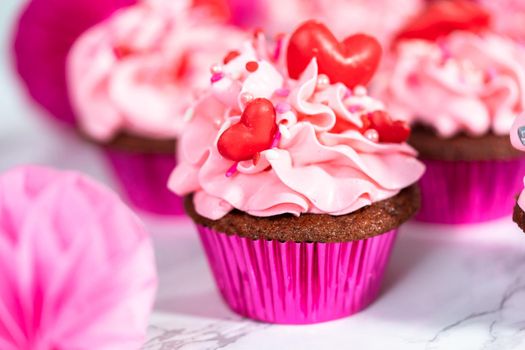 Red velvet cupcakes with pink Italian buttercream frosting and decorates with heart and kiss shaped red chocolates.