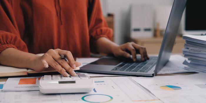 Business woman using calculator and laptop for do math finance on wooden desk in office and business working background, tax, accounting, statistics and analytic research concept.