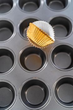Scooping cupcake batter with dough scoop into a baking cupcake pan with liners to bake dulce de leche cupcakes.