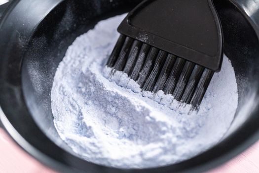 Hair color dye powder in a black plastic mixing bowl on a pink background.