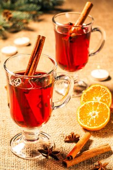 Glass of Christmas mulled wine with cinnamon, star anise and cloves on sackcloth with slices of orange, natural fir tree branches and cones. Color toning effect.