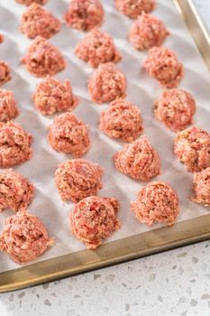 Scooping ground meat with dough scoop into a baking sheet lined with parchment paper to prepare oven-baked meatballs.