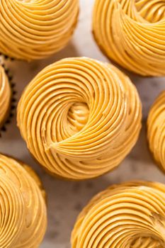 Piping dulce de leche buttercream frosting over vanilla cupcakes filled with caramel.