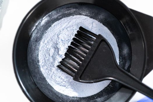 Hair color dye powder in a black plastic mixing bowl on a white background.