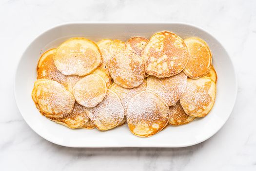 Freshly made small pancakes on a kefir base garnished with powdered sugar.