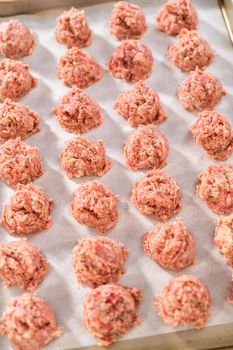 Scooping ground meat with dough scoop into a baking sheet lined with parchment paper to prepare oven-baked meatballs.