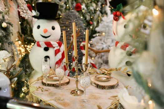 Snowmen sit at the Christmas table with the candles