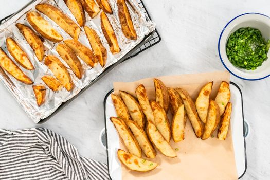 Flat lay. Freshly baked potato wedges with spices on a white serving tray.