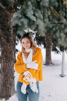 Teen blonde in a yellow sweater outside in winter. A teenage girl on a walk in winter clothes in a snowy forest.