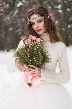 Beautiful bride in a white dress with a bouquet in a snow-covered winter forest. Portrait of the bride in nature.