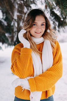 Teen blonde in a yellow sweater outside in winter. A teenage girl on a walk in winter clothes in a snowy forest.