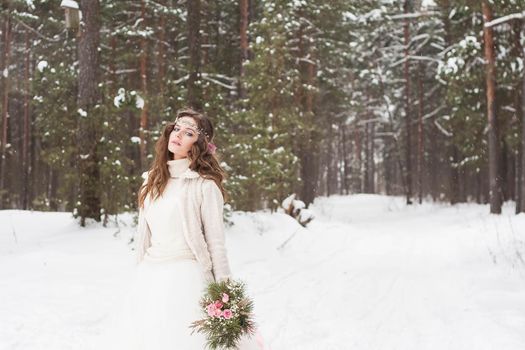 Beautiful bride in a white dress with a bouquet in a snow-covered winter forest. Portrait of the bride in nature.