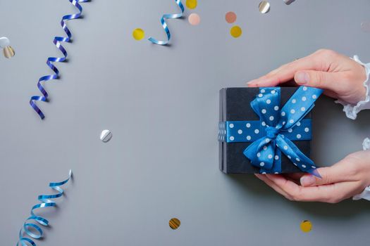 Female hands with black gift box and tinsel flat lay on grey background. Top view. High quality photo