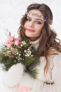 Beautiful bride in a white dress with a bouquet in a snow-covered winter forest. Portrait of the bride in nature.