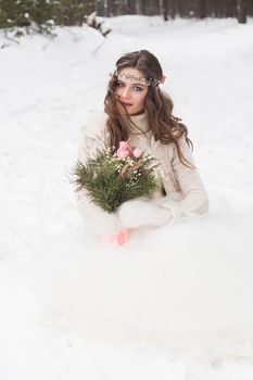 Beautiful bride in a white dress with a bouquet in a snow-covered winter forest. Portrait of the bride in nature.