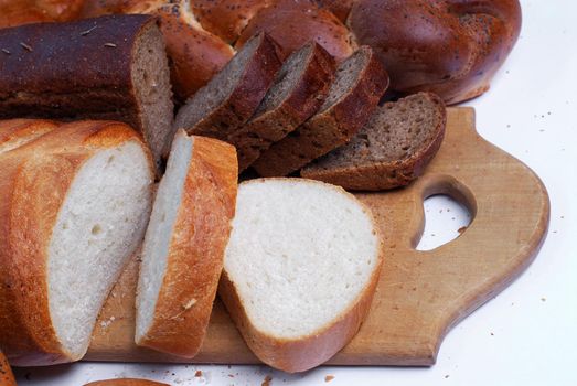 Bread lies on a wooden cutting board next to a knife on a white background.