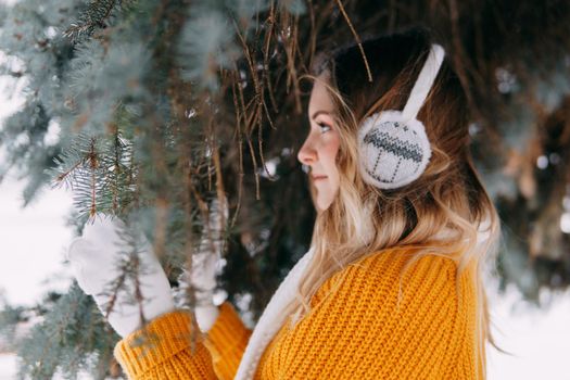 Teen blonde in a yellow sweater outside in winter. A teenage girl on a walk in winter clothes in a snowy forest.