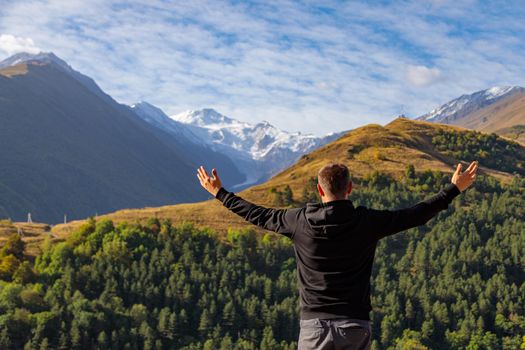 A man stands on top of a mountain with his arms outstretched
