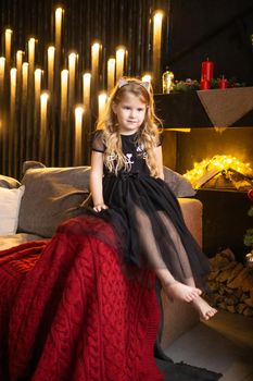 A girl in a festive outfit on the sofa with her dog next to a Christmas tree decorated with garlands, balloons and Christmas toys. The concept of winter holidays is Christmas and New Year holidays. Magical festive atmosphere.