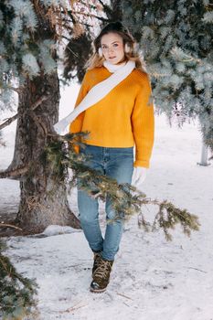 Teen blonde in a yellow sweater outside in winter. A teenage girl on a walk in winter clothes in a snowy forest.