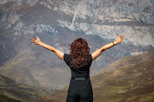 A young woman stands on top of a mountain with her arms outstretched