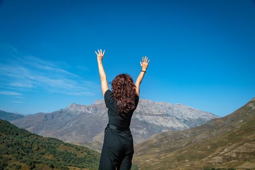A young woman stands on top of a mountain with her arms outstretched