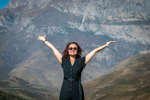 A young woman stands on top of a mountain with her arms outstretched