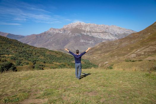 An adult man stands on top of a mountain with outstretched arms
