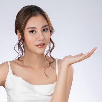 Photo of a gorgeous woman with flawless healthy fresh skin in a concept of empty space for beauty care product. Skincare product, model uses hand to create empty space for commercial.