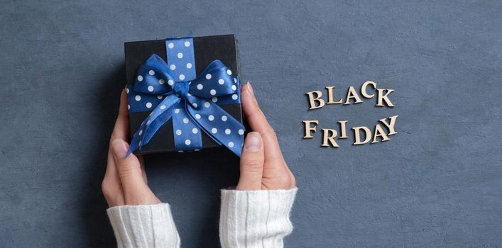 Banner with Black Friday text with gift in female hands flat lay on dark cement background. Top view.