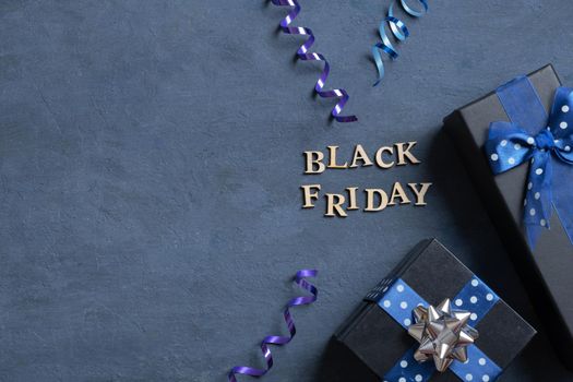 Black Friday text with gifts and holiday tinsel flat lay flat lay on dark cement background copy space. Top view.