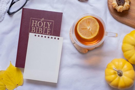 Holy Bible and blank sheet paper with autumn cozy decor top view.