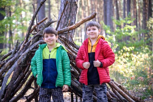 Two sibling brothers boys In the spring or autumn pine forest plays built a hut of sticks.