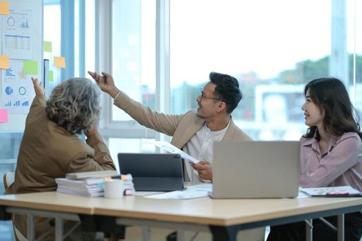 Group of Asian business people discuss together in team brainstorm meeting, work late night in office. Corporate business, coworker teamwork, financial consultant, or young entrepreneur concept.