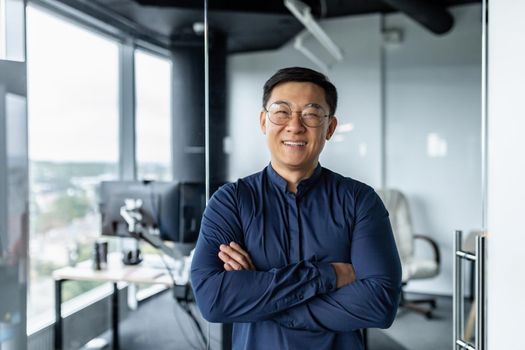 Portrait of successful asian businessman with crossed arms, businessman investor working inside office building loft, looking at camera and smiling, satisfied investor financier.