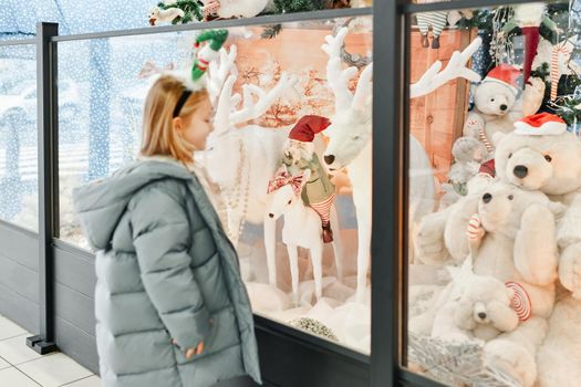 A child looks at a shop window with the toys for Christmas